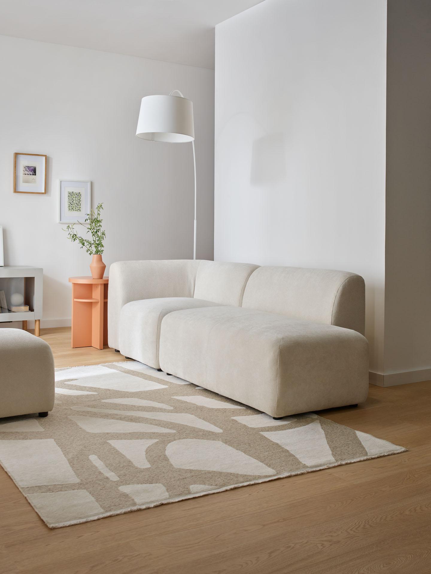 Minimalistyczna sofa z białą lampą na tle neutralnych ścian, dodających przestronności wnętrzu.