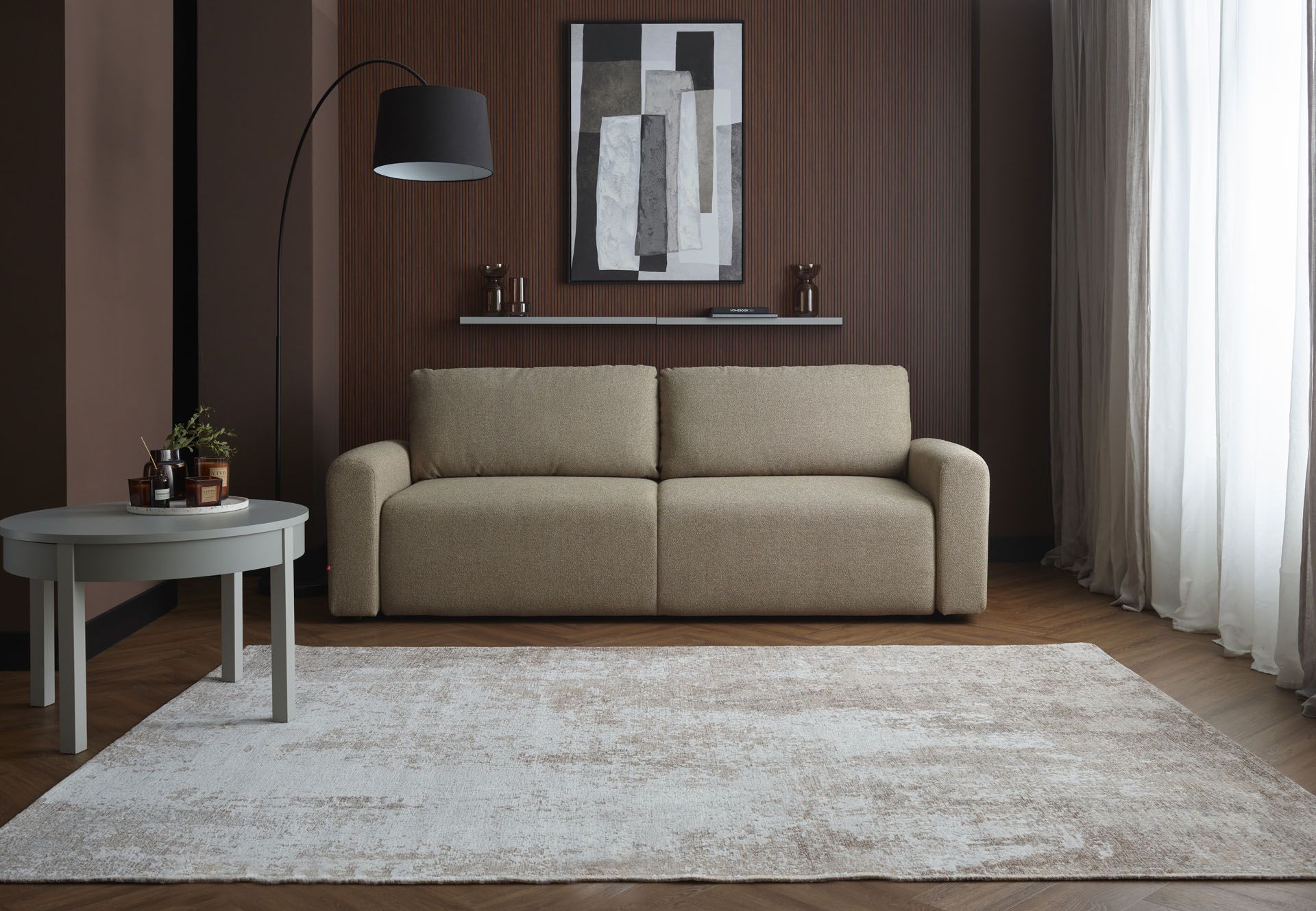 Oliwkowa sofa Fika na tle czekoladowej ściany