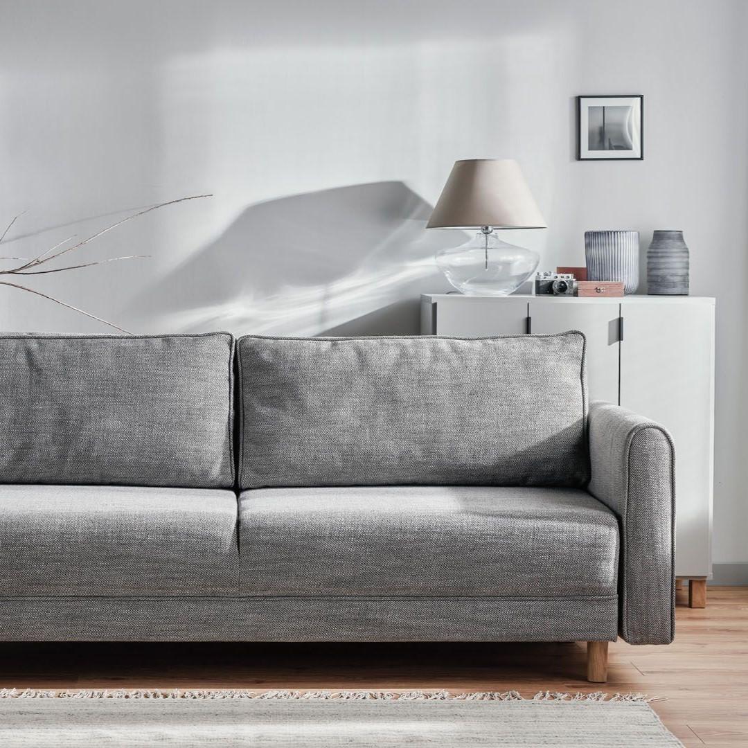 Szara sofa w jasnym salonie z delikatnymi dekoracjami.