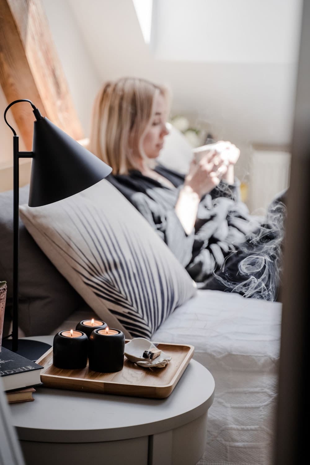 Kobieta leży na łóżku oparta o wezgłowie i trzyma kubek