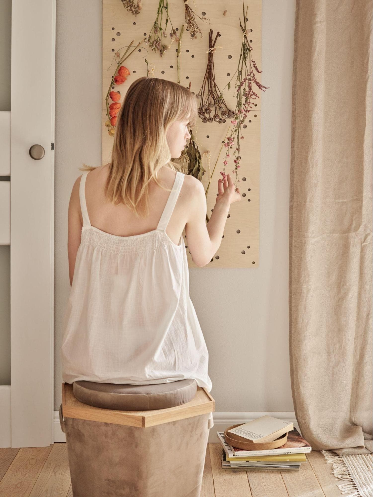 kobieta w przytulnej sypialni dekoruje drewnianą tablicę suszonymi ziołami i kwiatami