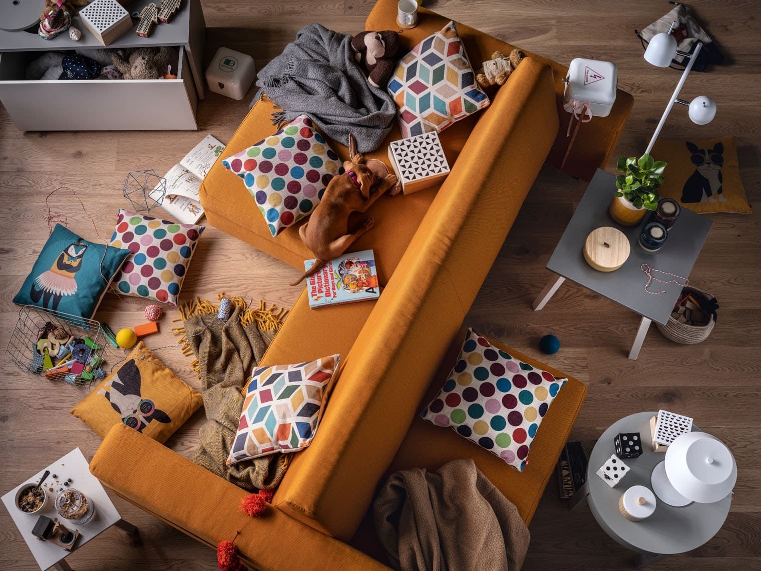 Dwustronna ruda sofa widziana z góry i rozrzucone kolorowe poduszki