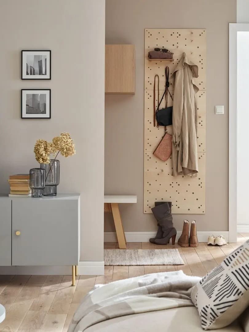 Przytulny kącik w przedpokoju z perforowaną tablicą ścienną do zawieszania akcesoriów, ławką i butami