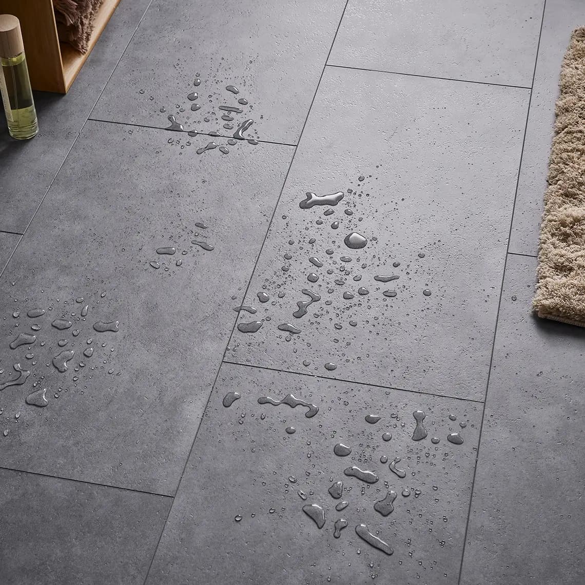 Zbliżenie na powierzchnię podłogi betonopodobnej w ciemnym odcieniu z kroplami wody, co podkreśla jej wodoodporne właściwości.